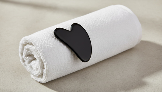 Gua sha in pietra nera su un asciugamano bianco arrotolato